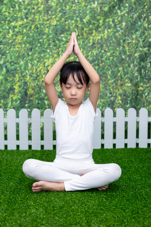 Asian Chinese little girl practicing yoga pose on a mat outdoorの写真素材