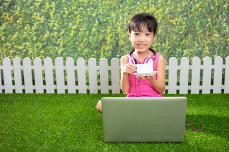 Asian Little Chinese girl sitting on the grass and playing with laptop at outdoor parkの写真素材