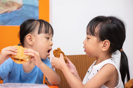 Asian Chinese little girl eating burger and fried chicken at indoor restaurantの写真素材