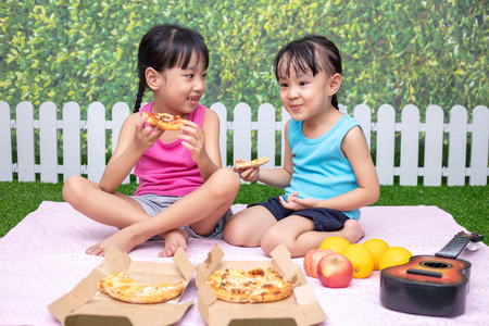 Asian Chinese little sisters eating pizza at outdoor gardenの写真素材