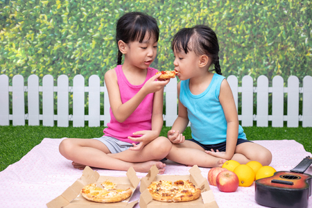 Asian Chinese little sisters eating pizza at outdoor gardenの写真素材
