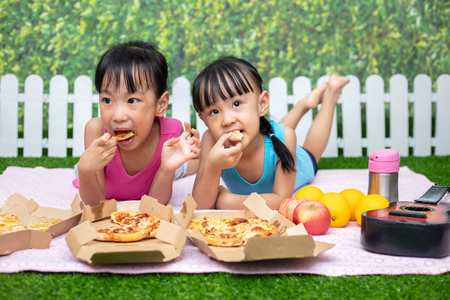 Asian Chinese little sisters eating pizza at outdoor gardenの写真素材