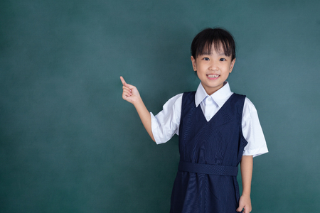 Asian Chinese little girl pointing with finger in front of green blackboardの写真素材