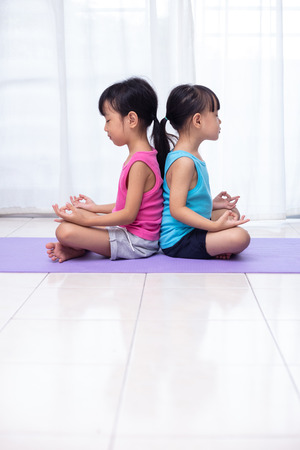 Asian Chinese little sisters practicing yoga pose on a mat in the living room at homeの写真素材