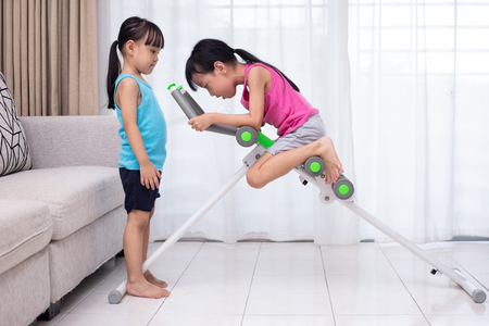 Asian Chinese little sisters playing workout machine in the living room at homeの写真素材