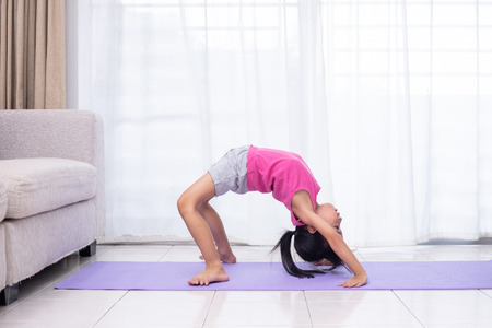 Asian Chinese little girl practicing yoga pose on a mat in the living room at homeの写真素材