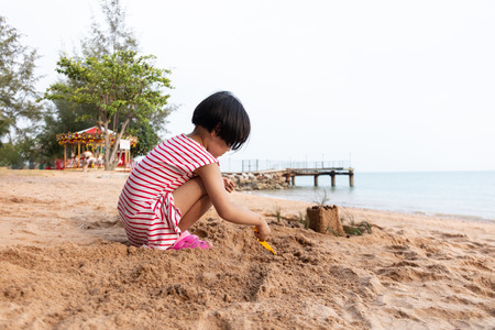Asian Chinese little girl playing sand at beach outdoorの写真素材
