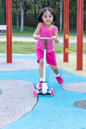 Asian little Chinese girl playing with scooter at outdoor parkの写真素材