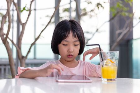 Asian Little Chinese Girl playing with tablet in the outdoor cafeの写真素材