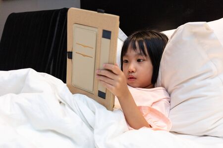 Asian Little Chinese Girl playing with tablet on bed at homeの写真素材