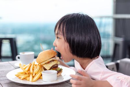 Asian Little Chinese Girl eating hamburger in the outdoor cafeの写真素材