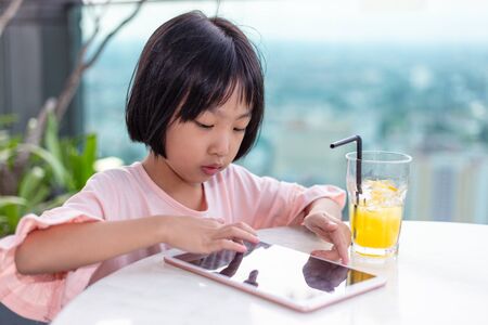 Asian Little Chinese Girl playing with tablet in the outdoor cafeの写真素材