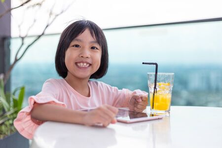 Asian Little Chinese Girl playing with tablet in the outdoor cafeの写真素材