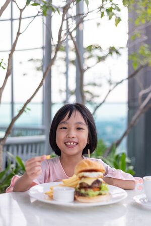 Asian Little Chinese Girl eating hamburger in the outdoor cafeの写真素材