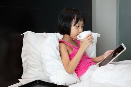 Asian Little Chinese Girl playing tablet in bed at homeの写真素材