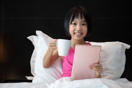 Asian Little Chinese Girl playing tablet in bed at homeの写真素材