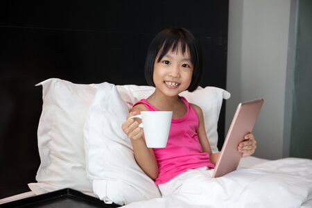 Asian Little Chinese Girl playing tablet in bed at homeの写真素材