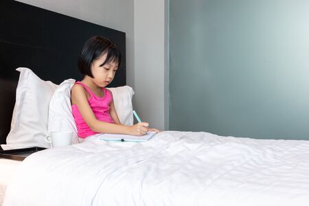 Asian Little Chinese Girl doing homework in bed at homeの写真素材