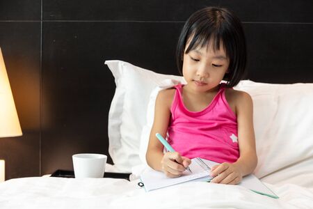 Asian Little Chinese Girl doing homework in bed at homeの写真素材