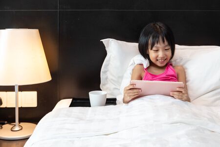Asian Little Chinese Girl playing tablet in bed at homeの写真素材