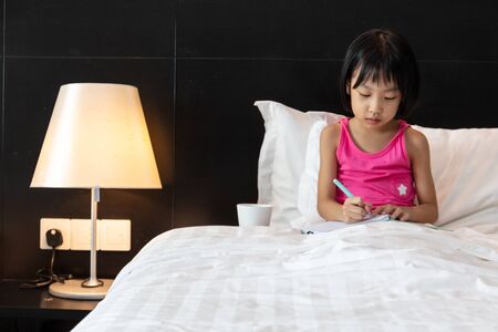 Asian Little Chinese Girl doing homework in bed at homeの写真素材