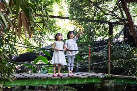 Asian Little Chinese Sisters standing on the wooden bridge at a gardenの写真素材