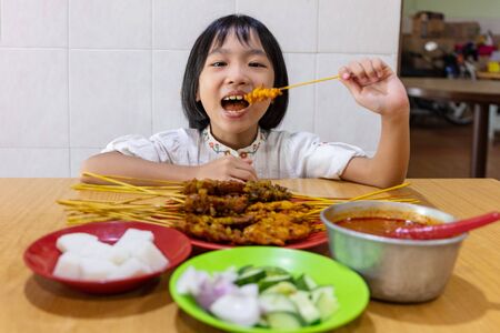 Asian Little Chinese Girl eating satay at an indoor restaurantの写真素材