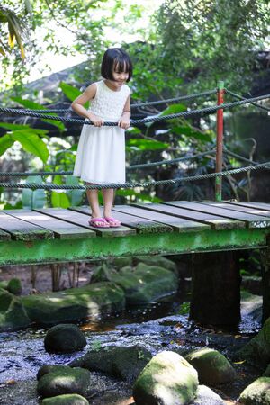 Asian Little Chinese Girl standing on the wooden bridge at a gardenの写真素材