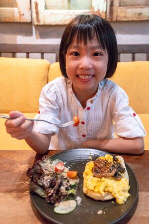 Asian Little Chinese Girl eating breakfast at an indoor cafeの写真素材