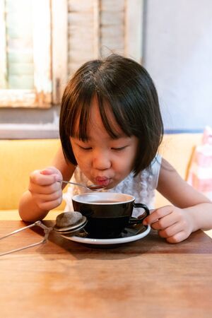 Asian Little Chinese Girl drinking hot tea at an indoor cafeの写真素材
