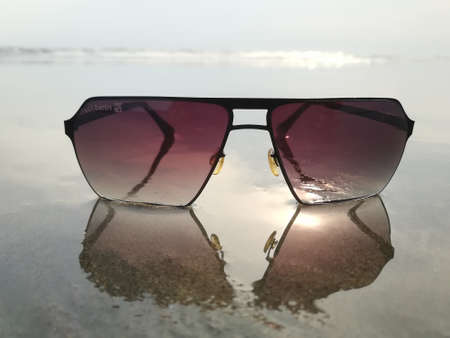 Sunglasses on the beach with reflection in water. Selective focus.の写真素材