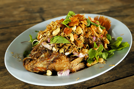 Fried Thai fish with Thai herb on the dish decorate on wooden table.