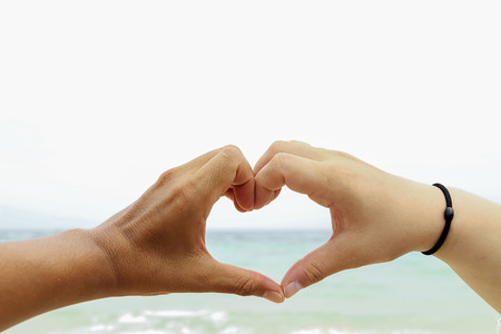 Love symbol by human hand at the beach and sky background in Thailand.の写真素材