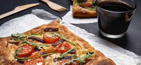 rectangular pizza with salami, tomatoes and rucola leaves and glass of coffee