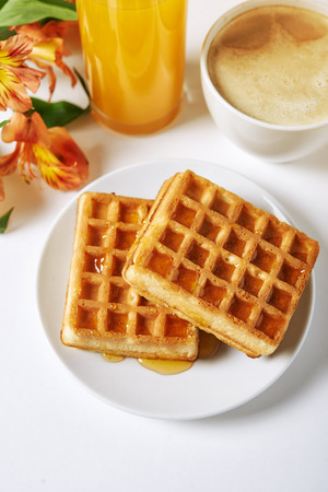 waffles, cappucino, juice and flowers on white tableの写真素材