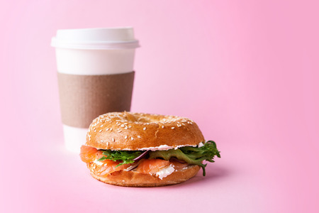 bagel with salmon and paper cup to go on pink backgroundの写真素材