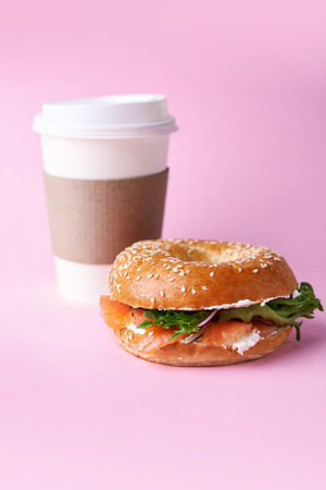 bagel with salmon and paper cup to go on pink backgroundの写真素材