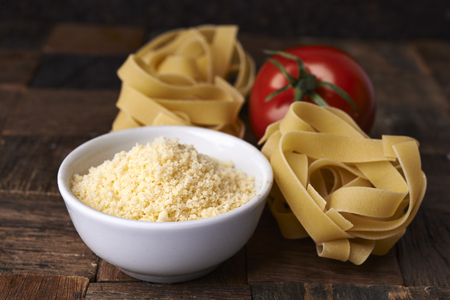 grated cheese and raw fettuccini on wooden backgroundの写真素材