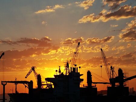 Sunset on a background of silhouettes from ship cranes arriving at the port.のeditorial素材