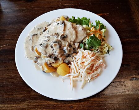 Two slices of cooked beef with mushroom sauce, boiled potatoes and fresh vegetable salad.