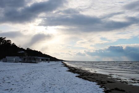 Winter sky with dark clouds and the sea coast covered with snow.の写真素材