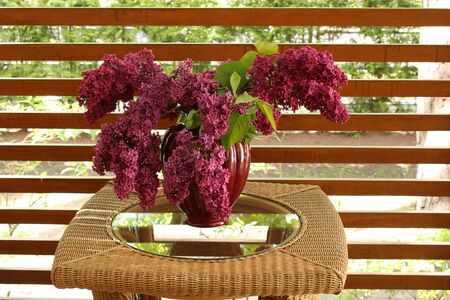 Beautiful bouquet of lilacs in a vase on a small wicker elegant table on the terrace.