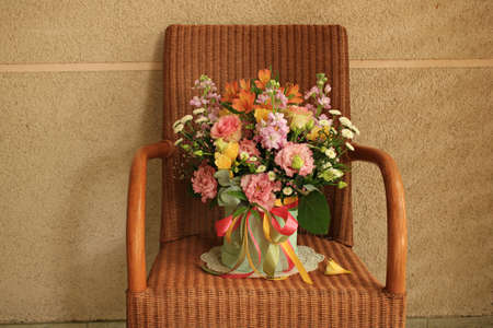 Bouquet with different types of beautiful flowers in vase on a wicker chair on the balconyの写真素材