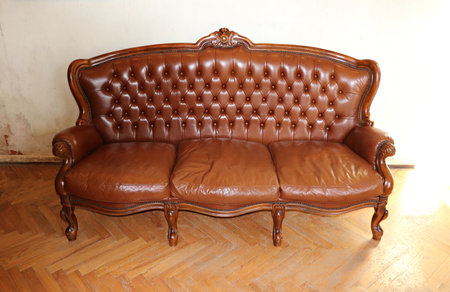Light brown leather vintage retro sofa by the wall in the room of an old house