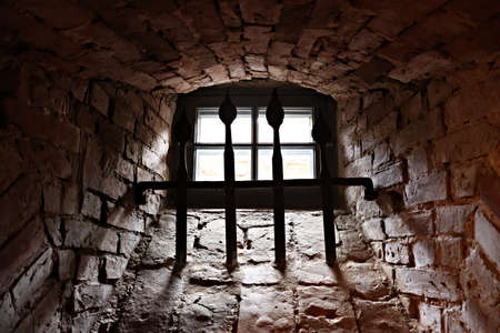 Window with a metal lattice in a thick stone wall of an underground room.