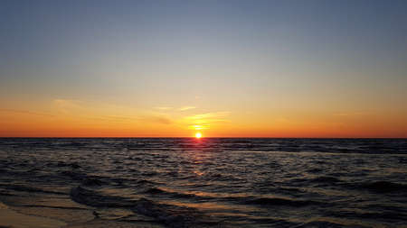 The sun in cloudless sky going beyond the horizon of the darkening sea.の写真素材