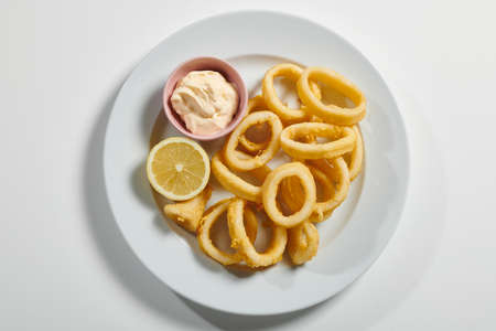 Plate of fried sliced ââsquid with mayonnaise sauce, lemon on white backgroundの写真素材