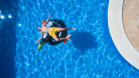 Child in yellow swimsuit sunbathing in the pool on a tucan-shaped matの写真素材