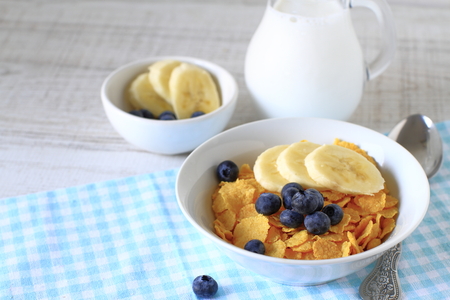 Breakfast cereal with blueberries, bananas and milk on a rustic wood table