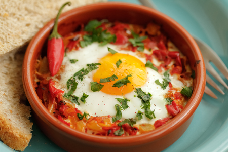 Eggs poached in tomato sauce and other vegetables served with bread.の写真素材
